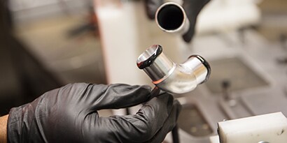 Learn about material bonding. Image of a metal pipe with adhesive about to be joint with a metal elbow joint.
